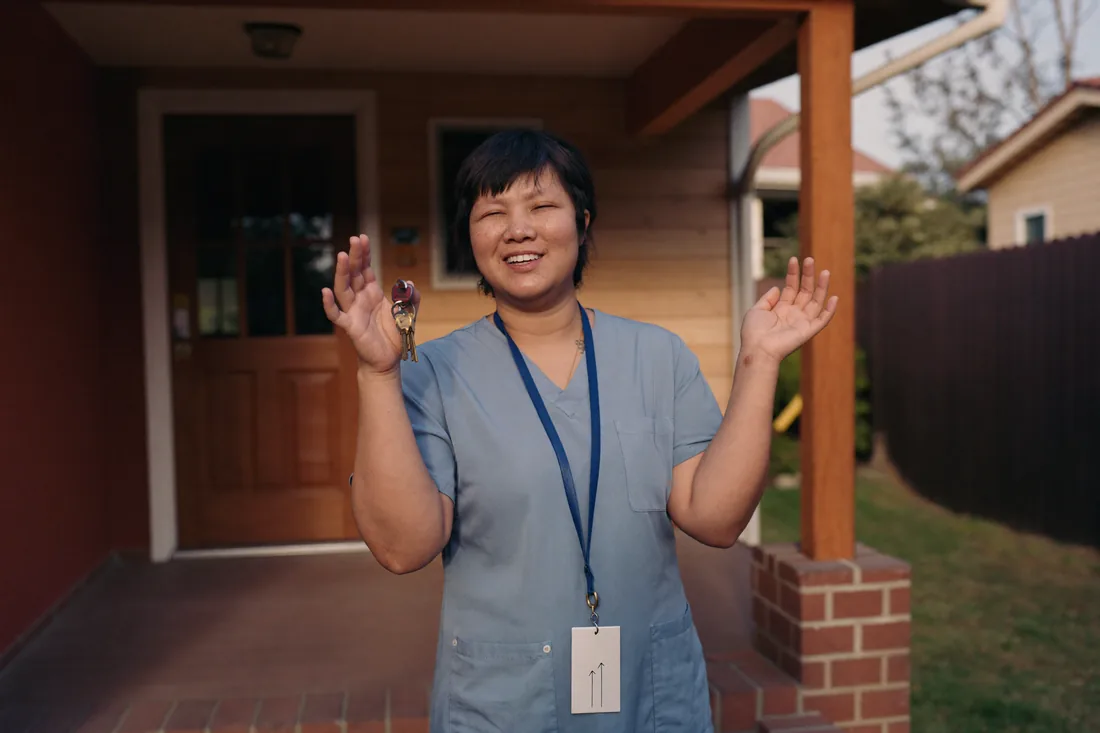 An Australian nurse in scrubs outside a suburban home, representing profession-based LMI waivers that lower effective home loan rates.