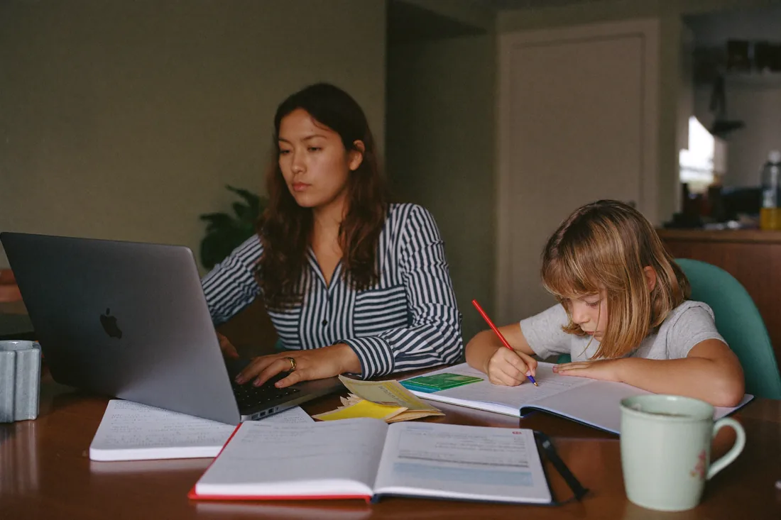 Single mother working out home loan deposit numbers at her kitchen table while her child does homework, Australia.
