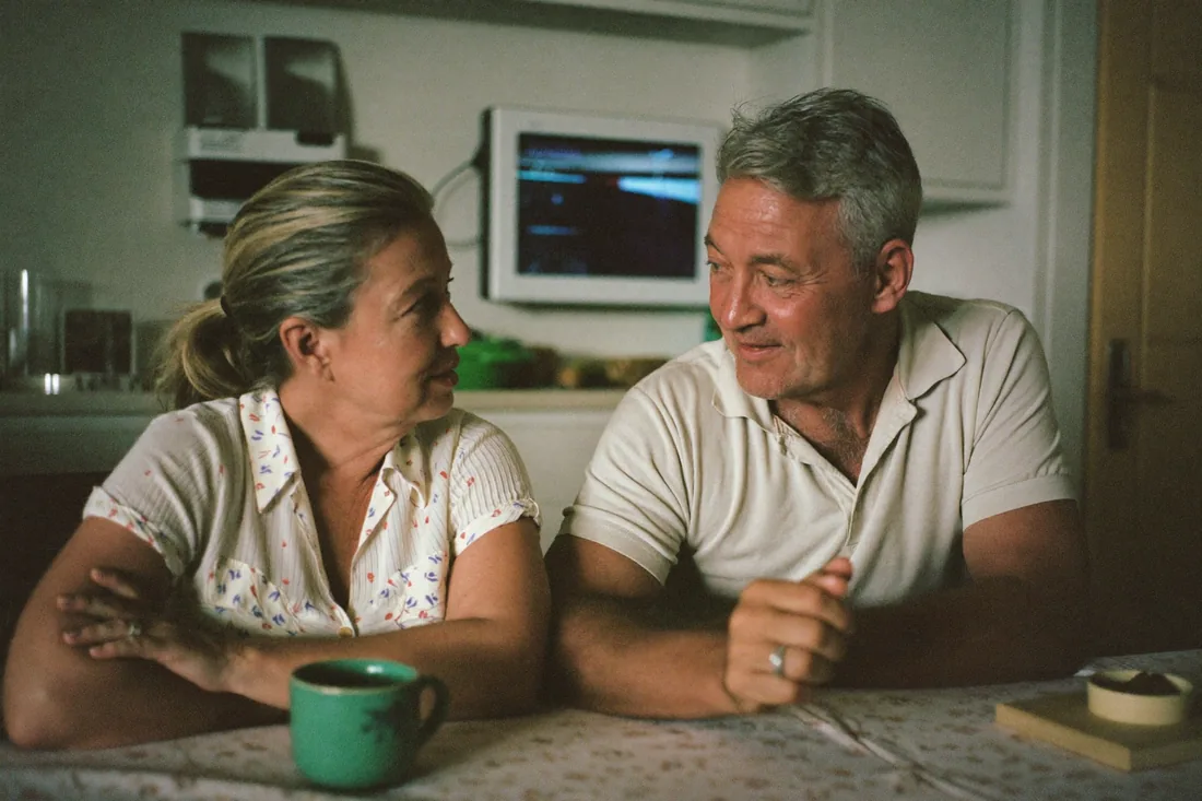 A middle-aged Australian couple sitting at their kitchen table, talking through whether to go guarantor on their child's home loan.
