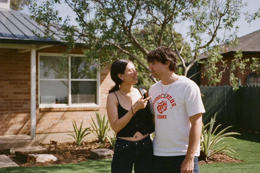 A young couple inspecting a suburban Australian home at an open-home inspection on a sunny day.