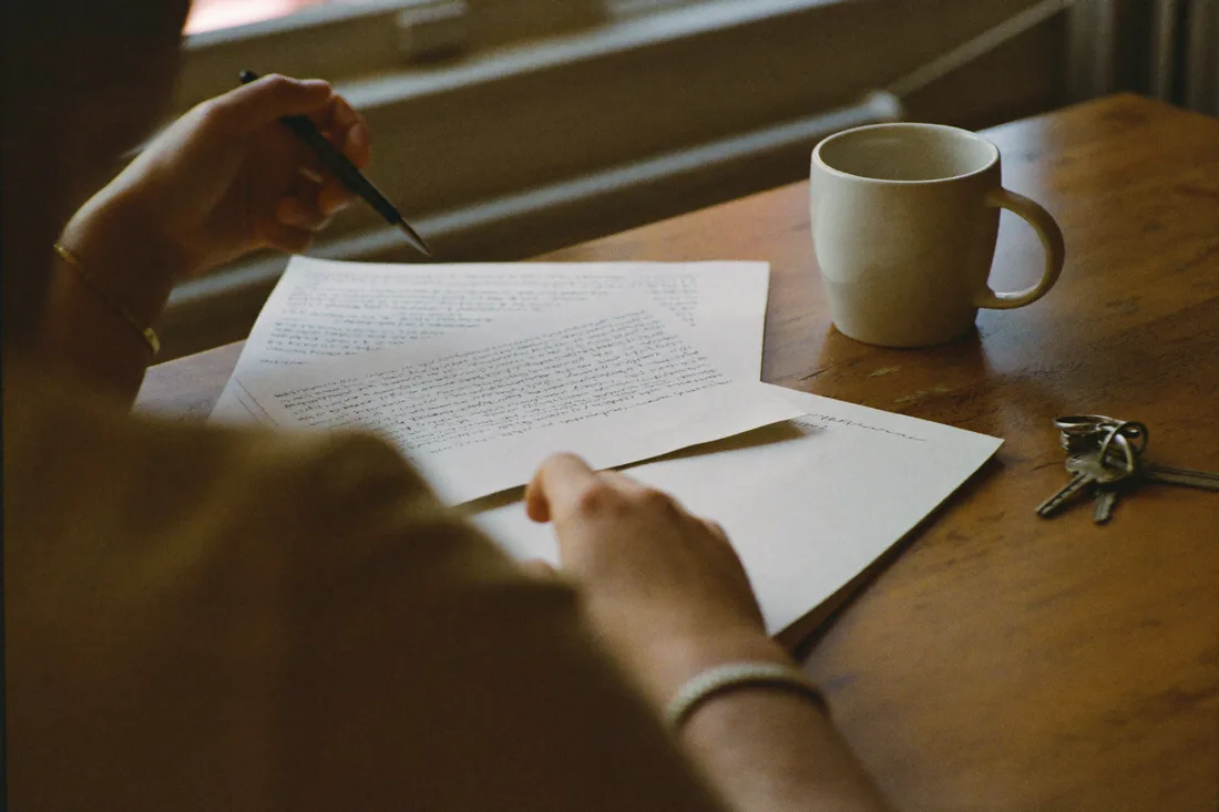 Hands resting on paperwork at a kitchen table with house keys and a coffee mug beside them.