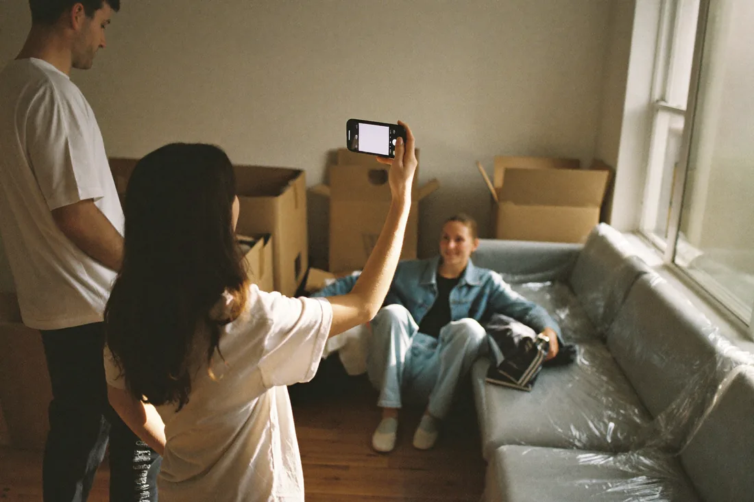 A young Australian couple recording a phone video of their belongings among moving boxes in a newly bought home to document contents for insurance.