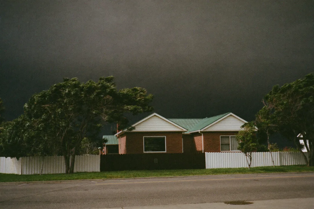 An Australian suburban home under a storm sky, illustrating weather risk to a property before settlement.