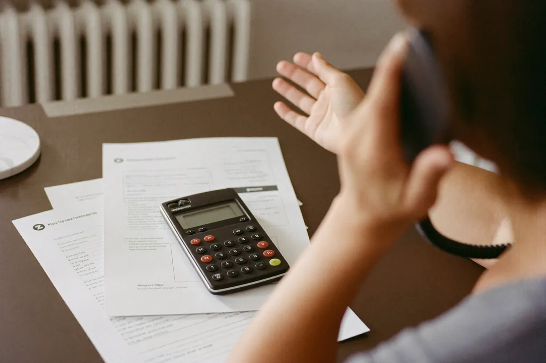 A first home buyer on the phone negotiating a home loan rate, with loan documents and a calculator on the desk.