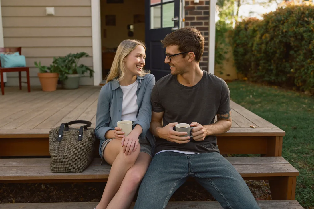 A first home buyer couple standing on the footpath outside their newly purchased suburban Australian home holding the keys.