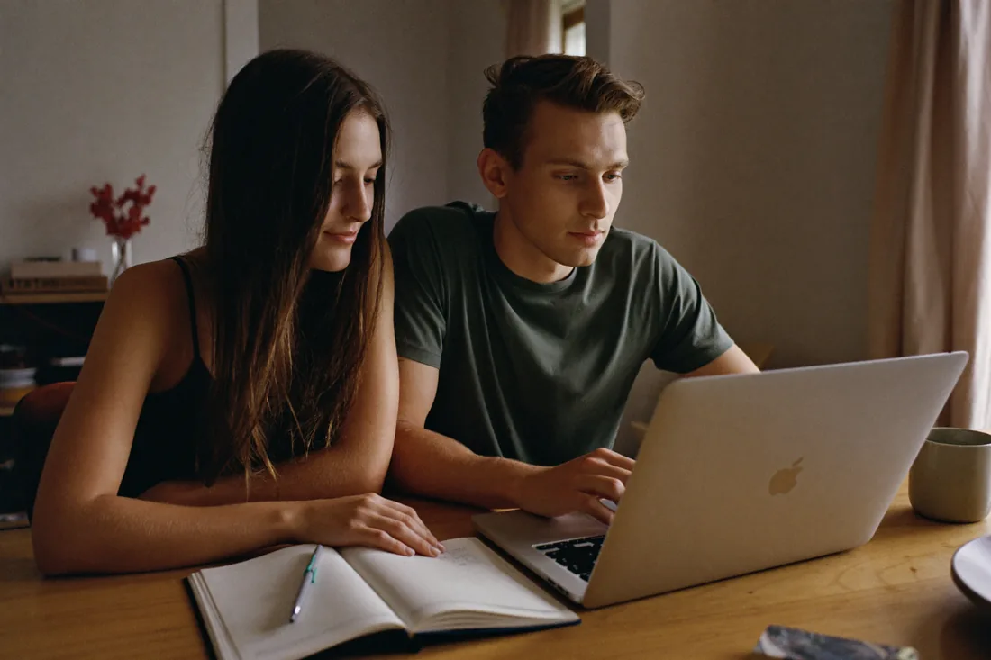A young Western Australian couple working out their home deposit at the kitchen table with a laptop and savings notes.