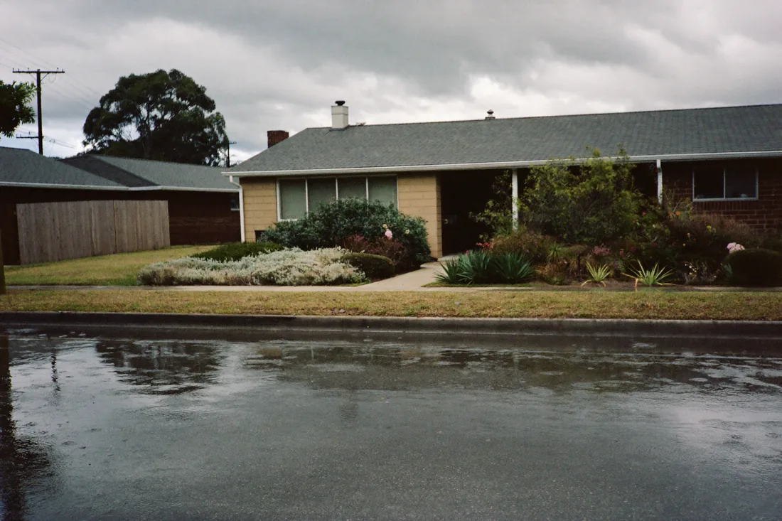 Rainwater pooling along the kerb and front yards of a low-lying Australian suburban street, showing why flood risk varies street by street.