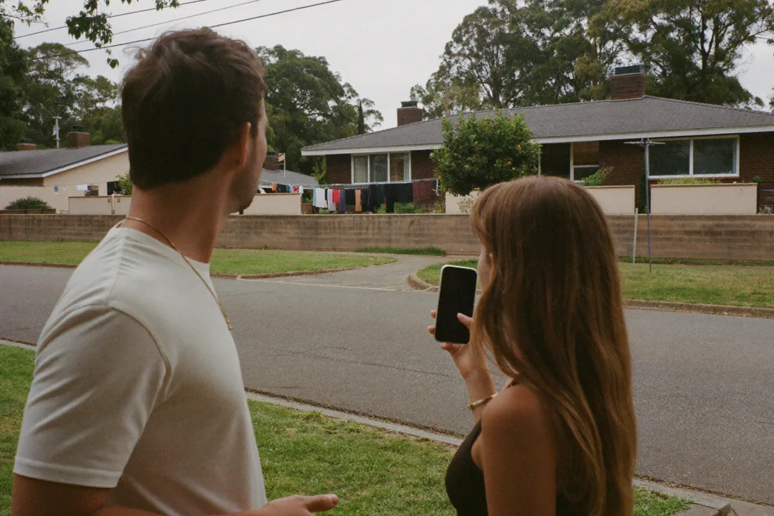 A young couple inspecting a house from the footpath during a weekend drive-by of an Australian suburb.