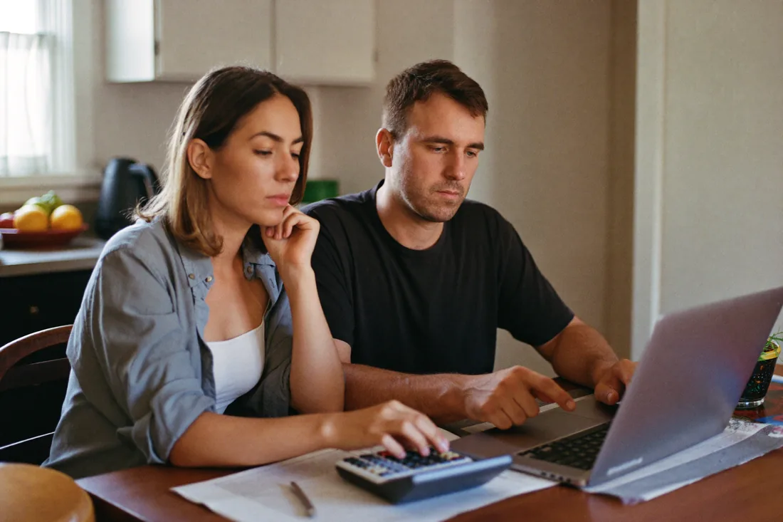 A young Australian couple at their kitchen table comparing interest only and principal and interest home loan repayments on a laptop.