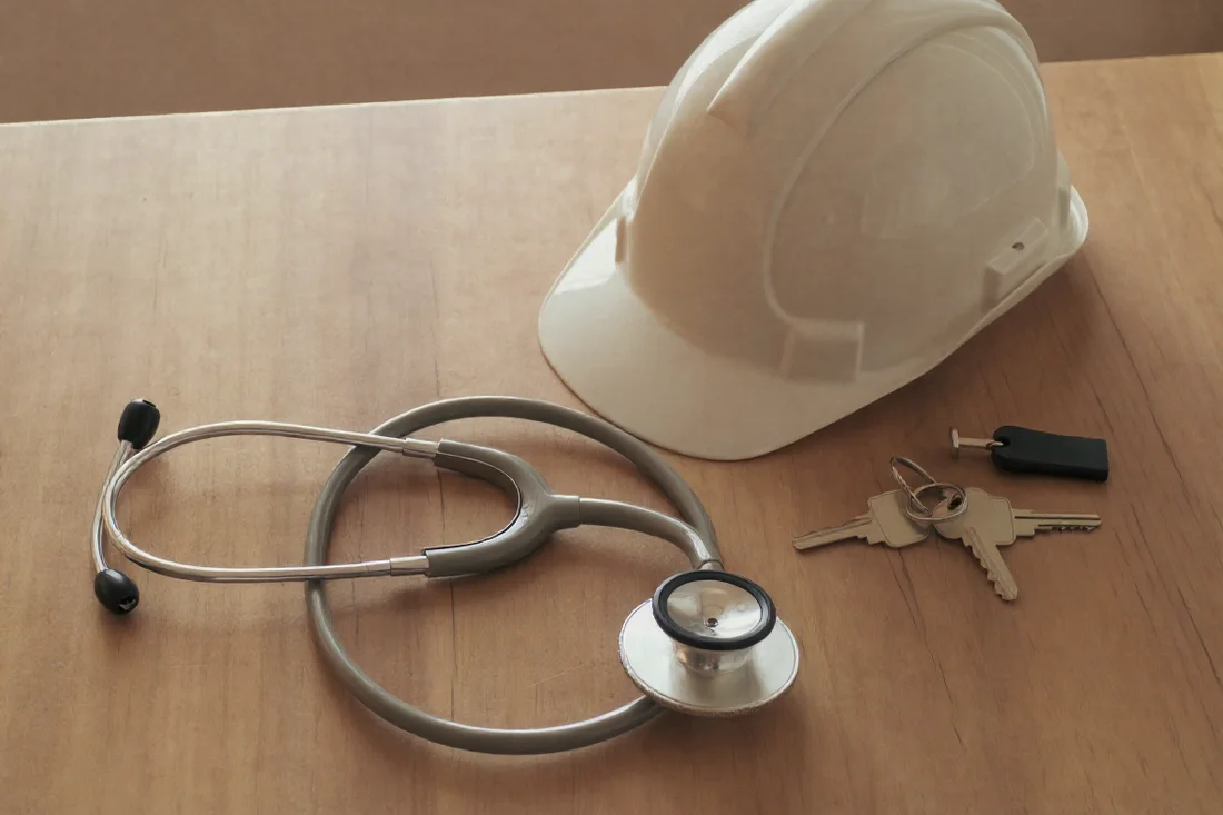 A stethoscope, a hard hat and a set of house keys laid out on a table.