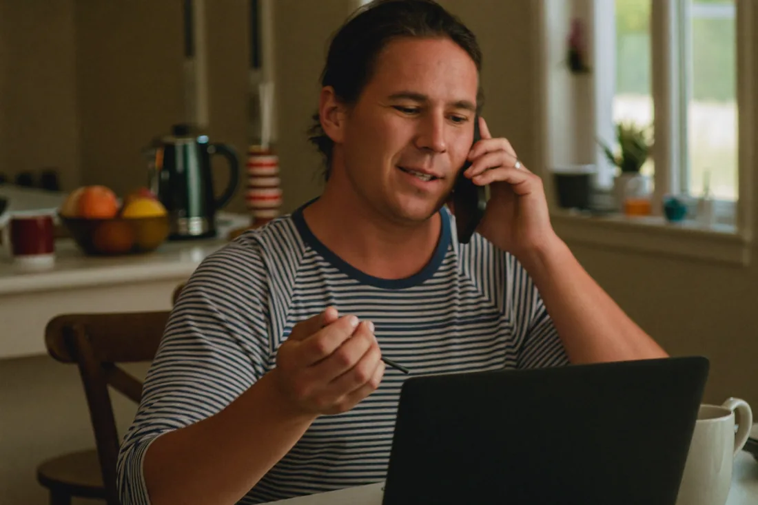 An Australian homeowner on the phone to their bank's retention team at the kitchen table while weighing up switching home loans.