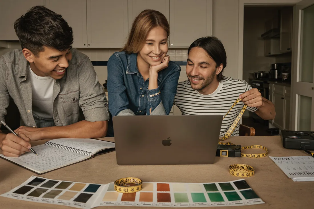 Australian homeowners planning their home renovation budget and finance options at a kitchen table with a laptop, paint swatches and a tape measure.