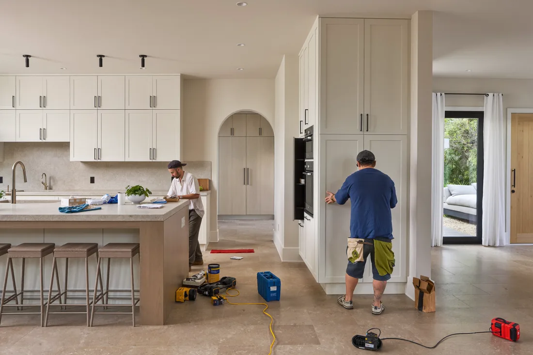 A modern Australian kitchen renovation in progress, showing new cabinetry and benchtops being installed by tradespeople.