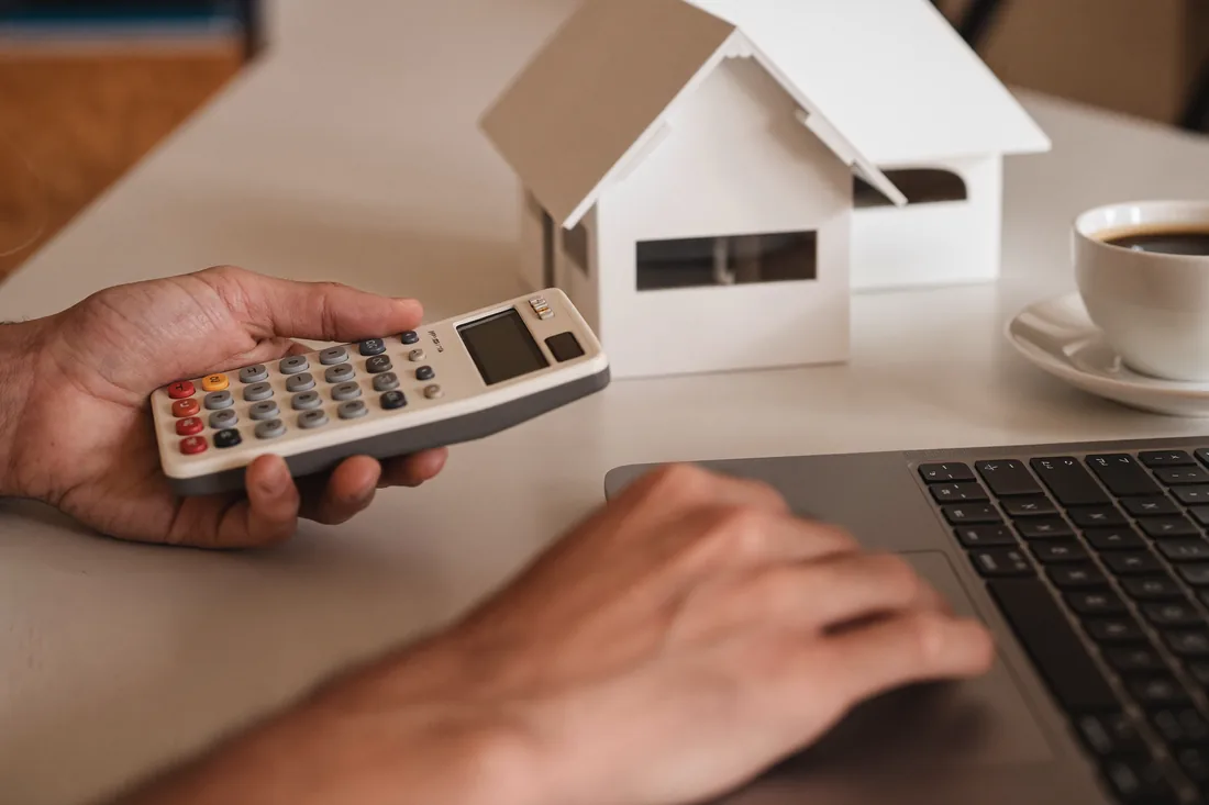 An Australian property investor calculating the rental yield on an investment property using a calculator and laptop at a desk.