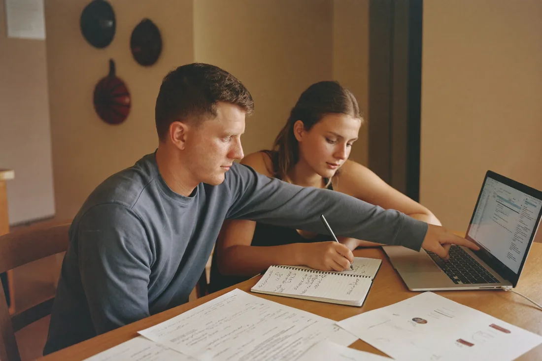 A young Australian couple working out rentvesting numbers at their kitchen table with a laptop and paperwork.